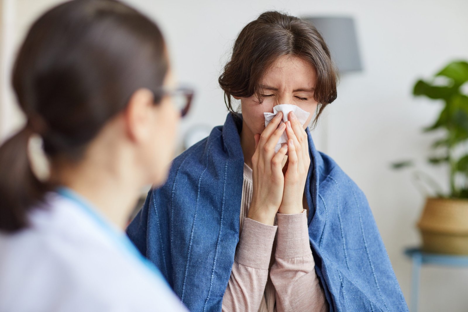 Sick woman caught a cold she has running nose and doctor sitting near by her and talking to her at home